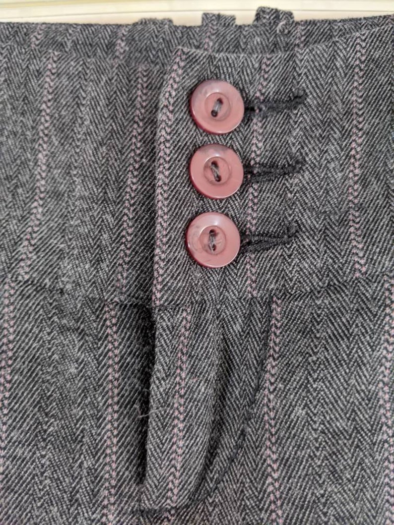 Peut inclure: Gros plan sur un tissu gris &agrave; chevrons avec des rayures roses verticales. Trois boutons roses sont visibles, cousus sur le tissu. Les boutons sont ronds et ont un bord l&eacute;g&egrave;rement sur&eacute;lev&eacute;. Le tissu semble &ecirc;tre une mati&egrave;re tiss&eacute;e.