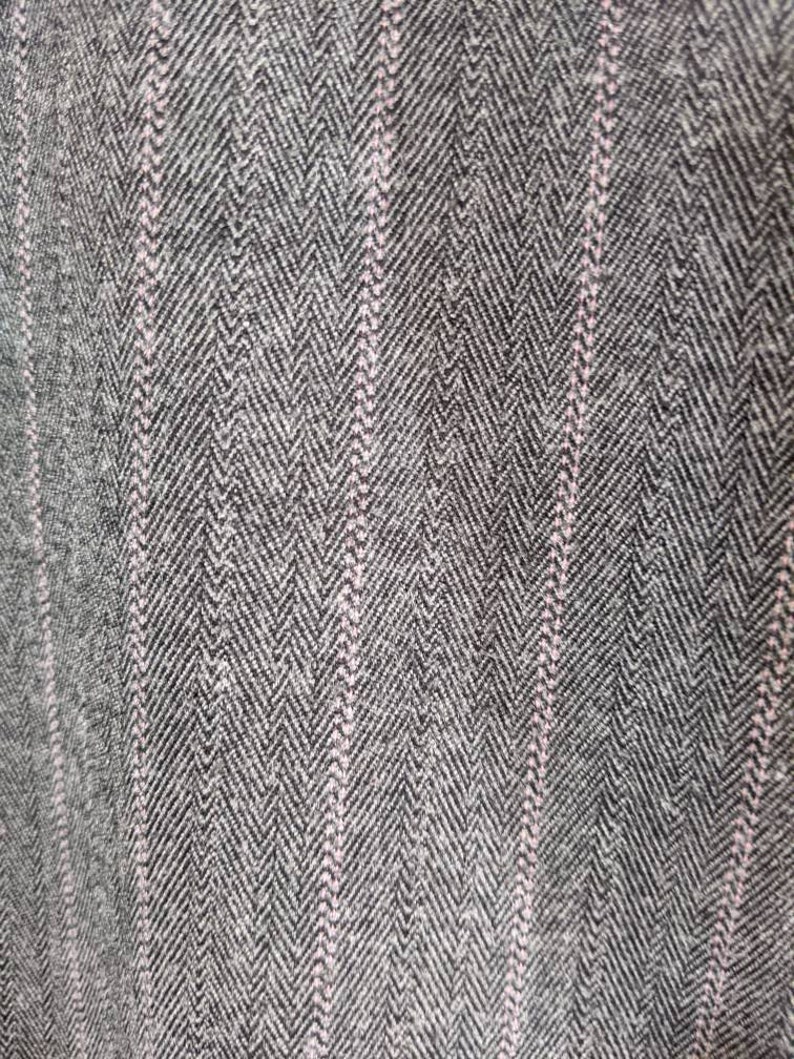 Peut inclure: Gros plan sur un tissu textur&eacute; avec un motif en chevrons dans des tons de gris et de noir. De fines rayures verticales rose clair traversent le motif, ajoutant un contraste subtil. Le tissu semble &ecirc;tre tiss&eacute;, sugg&eacute;rant un produit textile.