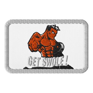 Puede incluir: Parche bordado con una figura musculosa naranja con detalles negros, flexionando sus músculos. El texto "GET SWOLE!" está en letras blancas estilizadas. El parche tiene un fondo blanco y un borde gris.