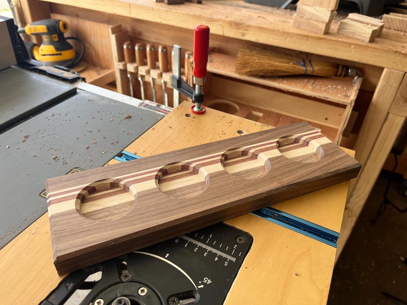 May include: A rectangular wooden flight board featuring four circular cutouts for glasses. The board is constructed from laminated strips of dark walnut, light maple, and reddish-brown wood, showcasing a striped pattern across the surface.