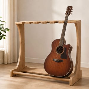 Pode incluir: Um suporte de guitarra de madeira castanho-claro com um trilho superior de várias ranhuras e uma barra de suporte na base, segurando uma guitarra acústica com corpo de madeira escura, pickguard preto e logótipo Taylor na cabeça.