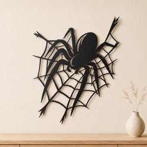 May include: A black wall-mounted spider and web decoration featuring a large, stylized arachnid with eight long, segmented legs positioned centrally on a geometric, interconnected web structure made of thin, dark, solid lines.