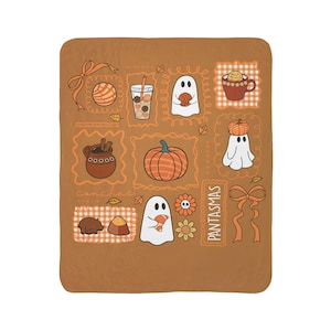 May include: A brown blanket featuring a variety of fall-themed illustrations in orange and white. The design includes a pumpkin, ghosts, a cup of coffee, and the text "PANTASMAS". The blanket is a cozy and decorative item.