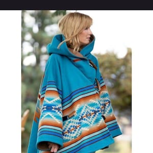 May include: A turquoise hooded poncho with a Southwestern design. The poncho features brown, orange, and blue geometric patterns and stripes. It has a toggle closure and a brown lining.