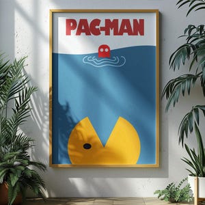 May include: A framed Pac-Man poster. The poster features a yellow Pac-Man character at the bottom, a red ghost in the middle, and the word "PAC-MAN" in red at the top. The background is blue and white. The poster is in a gold frame.
