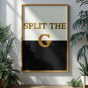 May include: A framed art print with a gold frame. The artwork is split horizontally, with a white top and a black bottom. Gold text reads "SPLIT THE G" with a large gold "G" in the centre.