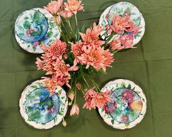May include: A bouquet of salmon-colored chrysanthemum flowers arranged in the center of four round ceramic plates. Each plate features a colorful, textured fruit pattern with green, red, and blue tones on a white background.