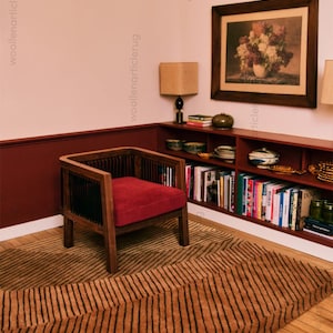May include: A room featuring a brown and black striped rug, a wooden armchair with a red cushion, and a bookshelf filled with books. A framed floral print hangs on the wall, and a lamp sits on the shelf. The room has a warm, inviting atmosphere.