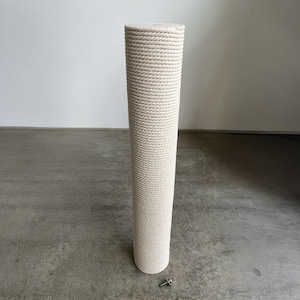 Puede incluir: Un poste rascador cilíndrico y alto, envuelto en una cuerda gruesa de fibra natural de color beige claro. El poste presenta una superficie superior e inferior plana, con un pequeño perno de metal en el suelo frente a la base de la estructura.