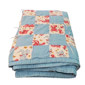 May include: A patchwork quilt featuring alternating squares of solid light blue fabric and a cream-colored fabric printed with red and blue cartoon animals, including rabbits, bears, and birds, with white fabric ties at the corners of the squares.