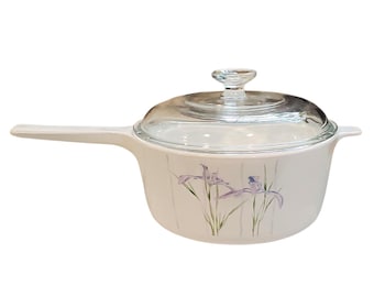 May include: White saucepan with a clear glass lid and a handle. The pan features a floral design of purple irises. A classic kitchenware item for cooking.