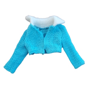 May include: A light blue knitted jacket with a white collar. The jacket has long sleeves and a V-neck design. The garment is made of a soft, textured material, and is likely for a doll or small figure.