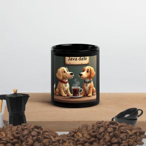 Può includere: Tazza da caffè nera con un'illustrazione a cartoni animati di due cani in un "Java date". I cani sono seduti a un tavolo con una tazza di caffè. La tazza ha anche il testo "Java date".