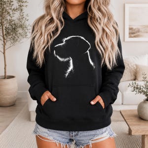 Può includere: Felpa con cappuccio nera con una silhouette bianca della testa di un cane. La felpa ha una tasca frontale e un cappuccio con coulisse. Il profilo del cane è dettagliato in bianco. Abbigliamento casual.
