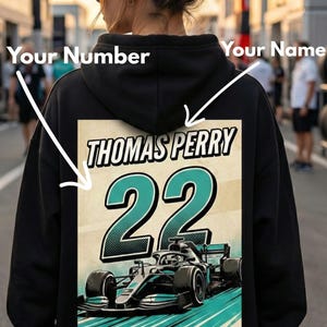 Może przedstawiać: Czarna bluza z kapturem z grafiką z napisem "THOMAS PERRY", numerem "22" i projektem samochodu wyścigowego. Projekt ma turkusowe i białe akcenty na beżowym tle.