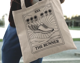 May include: Beige canvas tote bag featuring a black and white illustration of a winged running shoe, sunflowers, and the text "THE RUNNER". The bag has a rectangular design with a handle.