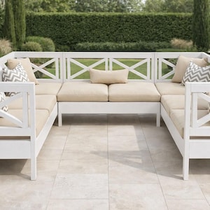 May include: A white outdoor sectional sofa with beige cushions and decorative pillows. The sofa has an X-shaped design on the back and sides. The background features greenery and a stone patio.