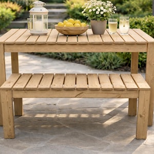 May include: A light brown wooden outdoor table and bench set. The table has a slatted top and a lower shelf. A wooden bowl of lemons, a potted plant, and drinks sit on the table. A lantern is also on the table.