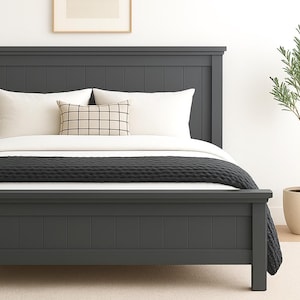 May include: A dark gray bed frame with a matching headboard. The bed is made up with white bedding, a black blanket, and decorative pillows. A potted plant is to the right of the bed.