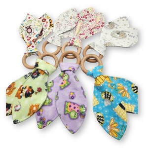 May include: A collection of baby teething toys with wooden rings and colorful fabric attachments. The fabric features various patterns, including floral, animal, and geometric designs. The toys are designed for infants and toddlers.