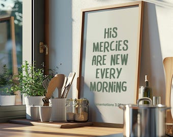 May include: A kitchen scene featuring a framed print with the words "His Mercies Are New Every Morning" in green. Wooden utensils, jars, and a potted plant are visible. A stainless steel saucepan sits in the foreground.
