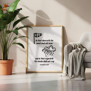 May include: A framed print with a wooden frame featuring black line art of a windsock, rain cloud, and text from Ecclesiastes 11:4. The print is displayed near a potted plant and a gray armchair with a blanket.
