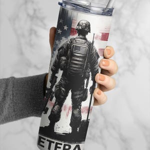 Puede incluir: Vaso de acero inoxidable con una ilustración en blanco y negro de un soldado y la bandera estadounidense. La palabra "ETERA" está impresa en la parte inferior. Incluye una tapa transparente y una pajita blanca.
