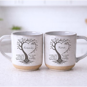 Puede incluir: Dos tazas de cerámica con un diseño de árbol, cada una con un dosel en forma de corazón y los nombres "Frank" y "Rose". Las tazas tienen una base de color beige claro y el texto "Every love story is beautiful, but ours is my favorite."