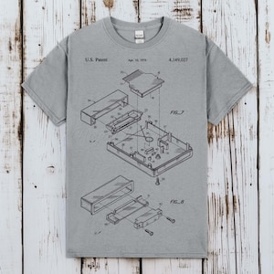Könnte beinhalten: Ein kurzärmeliges T-Shirt in Grau meliert mit einer schwarzen technischen Strichzeichnung eines US-Patents vom 10. April 1979, Patentnummer 4.149.027. Die Grafik zeigt Explosionszeichnungen mit der Beschriftung FIG. 7 und FIG. 8 sowie nummerierte Teile.