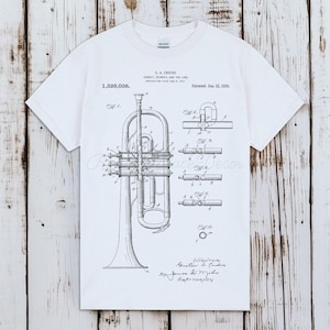 May include: White t-shirt featuring a detailed black and white diagram of a cornet, trumpet, and the like. The diagram includes various parts of the instrument, with text and patent information. The shirt has a classic crew neck and short sleeves.