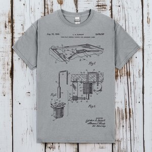 Może przedstawiać: Szary t-shirt z krótkim rękawem z czarną techniczną ilustracją patentową zatytułowaną Aug. 23, 1949, L.A. Durant, 2,479,707, Free-Play Control Circuit for Amusement Games. Grafika zawiera szczegółowe schematy oznaczone jako Fig. 1 oraz Fig. 2.