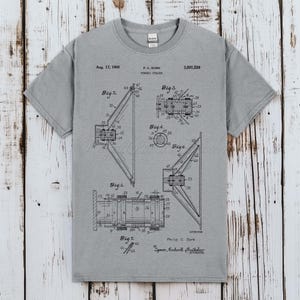 Könnte beinhalten: Ein graues Kurzarm-T-Shirt mit einer schwarzen technischen Patentzeichnung eines Lautsprecherdesigns. Der Aufdruck enthält den Text Aug. 17, 1965, P. C. SURH, 3,201,529, Dynamic Speaker, Fig. 2, Fig. 3, Fig. 4, Fig. 5, Fig. 6, Fig. 7 und Philip C. Surh.