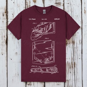 Op de afbeelding: Een bordeauxrood t-shirt met korte mouwen en een witte grafische print van een Amerikaans patent uit 9 mei 1989, met patentnummer 4.828.263. Het ontwerp toont technische lijntekeningen met de labels Fig. 1, Fig. 2 en Fig. 3c met genummerde delen.