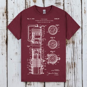 May include: Burgundy t-shirt featuring a white schematic diagram of a distillation apparatus, with detailed technical drawings and text. The text includes dates, patent information, and the inventor's name. A unique design for science enthusiasts.