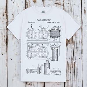 May include: White t-shirt featuring a black and white diagram of a beer-making process, including barrels, tanks, and pipes. The text on the shirt reads "O. & O. B. ZWIETUSCH. PROCESS OF MAKING BEER. Patented Jan. 17, 1893."