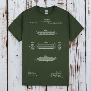 以下が含まれることがあります： 白いハーモニカの図が描かれた、濃い緑色のTシャツ。「J. Hohner, Mouth Harmonica, Patented Aug. 24, 1897」と書かれています。シャツには特許番号588,920も含まれています。
