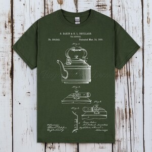 May include: An olive green short-sleeved t-shirt featuring a white screen-printed patent illustration of a tea kettle. The graphic includes technical drawings labelled Fig. 1, Fig. 2, Fig. 3, and Fig. 4, along with the text G. Dakin & H. L. Drullard.