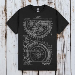 Pode incluir: Camiseta preta com um diagrama de engrenagem mecânica branco. O diagrama inclui esquemas detalhados, informações de patente e o número 1.024.897. A camiseta é de gola redonda, perfeita para quem se interessa por engenharia ou design industrial.