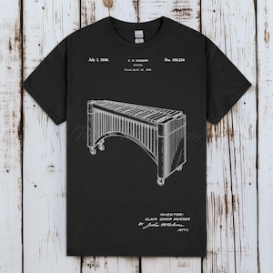 以下が含まれることがあります： 黒いTシャツ。マリンバの詳細なイラストが描かれており、1936年7月7日の日付と発明者Clair Omar Musserが記載されています。デザインはヴィンテージの青写真スタイルで、テキストが含まれています。