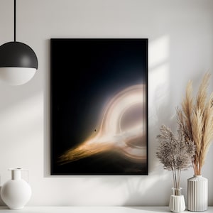 May include: A framed art print depicting a black hole. The image features a bright, swirling vortex of light and color against a dark background. The artwork is framed in a black border and is displayed on a white surface.