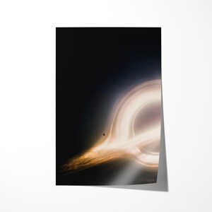 May include: A poster featuring a depiction of a black hole. The image shows a bright, swirling ring of light against a dark background. A small, dark sphere is visible near the center of the ring. The poster is rectangular and has a glossy finish.