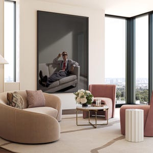 May include: A modern living room with a large framed artwork featuring a person on a sofa. The room includes two curved armchairs, a small round table, and a side table. The color palette is neutral with pink and beige accents.