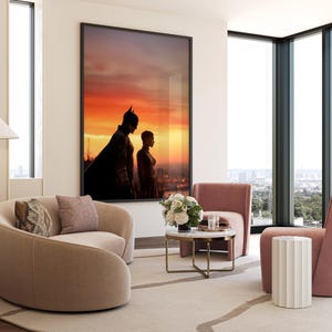 Puede incluir: Una impresi&oacute;n art&iacute;stica enmarcada con Batman y Catwoman silueteados contra un atardecer vibrante. La obra de arte cuelga sobre un sof&aacute; beige curvo con cojines decorativos. La habitaci&oacute;n incluye una peque&ntilde;a mesa redonda de m&aacute;rmol, sillones rosas y una mesa auxiliar blanca.