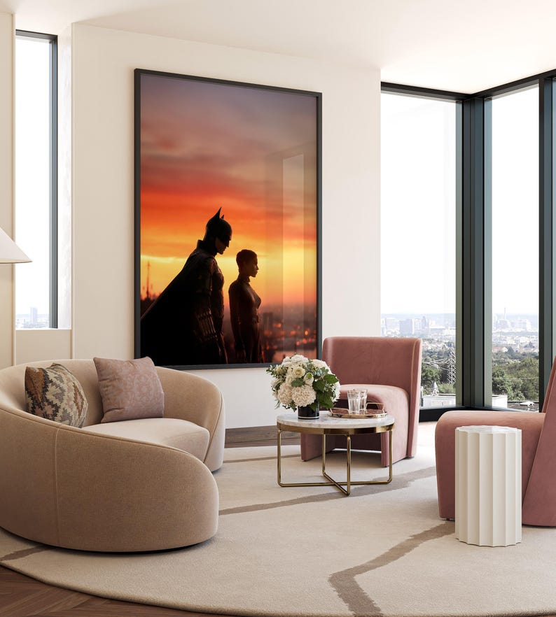 Puede incluir: Una impresi&oacute;n art&iacute;stica enmarcada con Batman y Catwoman silueteados contra un atardecer vibrante. La obra de arte cuelga sobre un sof&aacute; beige curvo con cojines decorativos. La habitaci&oacute;n incluye una peque&ntilde;a mesa redonda de m&aacute;rmol, sillones rosas y una mesa auxiliar blanca.