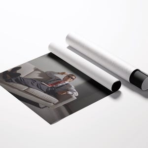 May include: A print of a person lying on a couch, with two white poster tubes. The print shows a person wearing a suit and sunglasses. The tubes are white with black end caps.