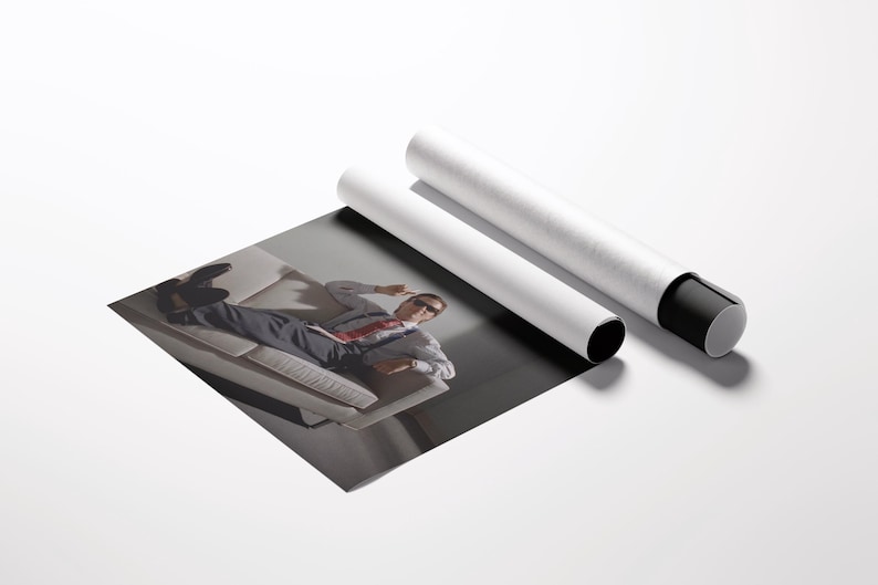 May include: A print of a person lying on a couch, with two white poster tubes. The print shows a person wearing a suit and sunglasses. The tubes are white with black end caps.