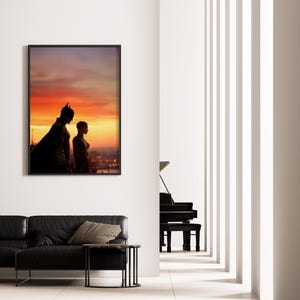 Puede incluir: Obra de arte enmarcada con siluetas de Batman y Catwoman contra un vibrante atardecer. La imagen se exhibe en una pared blanca sobre un sof&aacute; de cuero negro, realzando la est&eacute;tica moderna de la habitaci&oacute;n. Un piano de cola es visible en el fondo.
