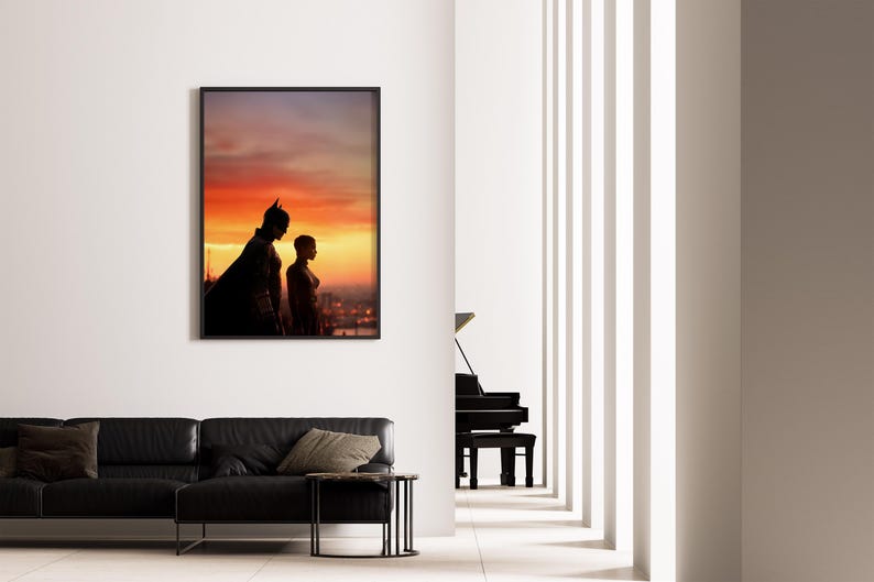 Puede incluir: Obra de arte enmarcada con siluetas de Batman y Catwoman contra un vibrante atardecer. La imagen se exhibe en una pared blanca sobre un sof&aacute; de cuero negro, realzando la est&eacute;tica moderna de la habitaci&oacute;n. Un piano de cola es visible en el fondo.