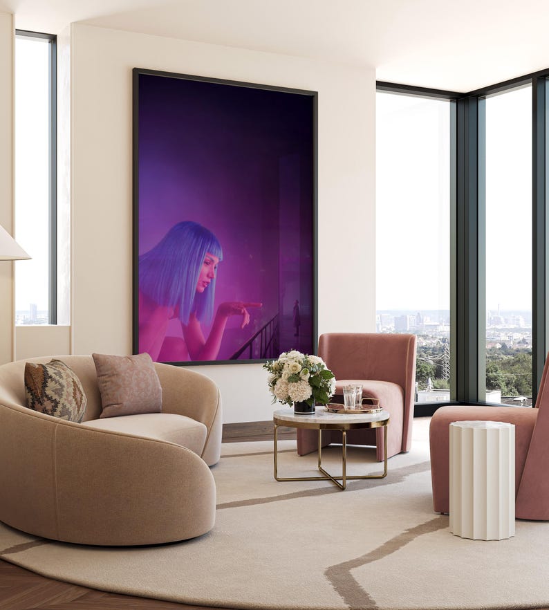 May include: A modern living room with a large framed artwork featuring a woman with blue hair. The room includes two curved beige sofas, two pink armchairs, a marble-topped coffee table, and a white side table. A large window offers a city view.