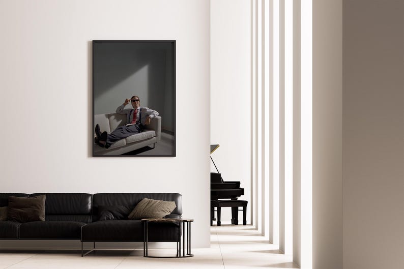 May include: A framed artwork depicts a person in a suit and sunglasses lounging on a sofa. The room features a black leather sofa, a side table, and a grand piano. The interior has a minimalist design with white walls and vertical architectural elements.